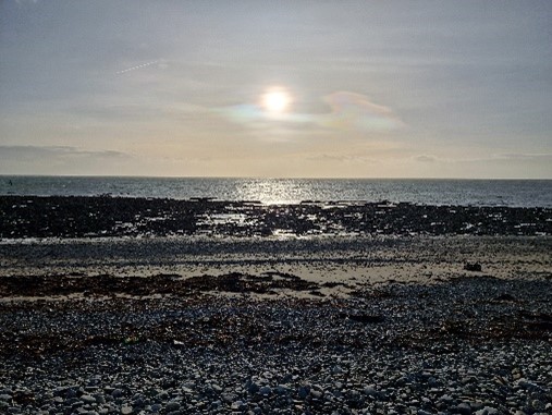 An image taken from the beach, pointing at the sea with the sun setting in the middle of the sky